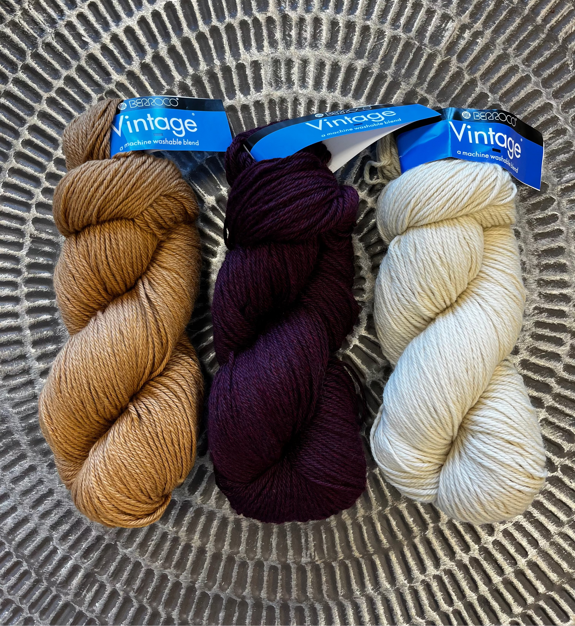 Three skeins of yarn in brown, purple, and cream on a textured surface with 'Vintage' labels.